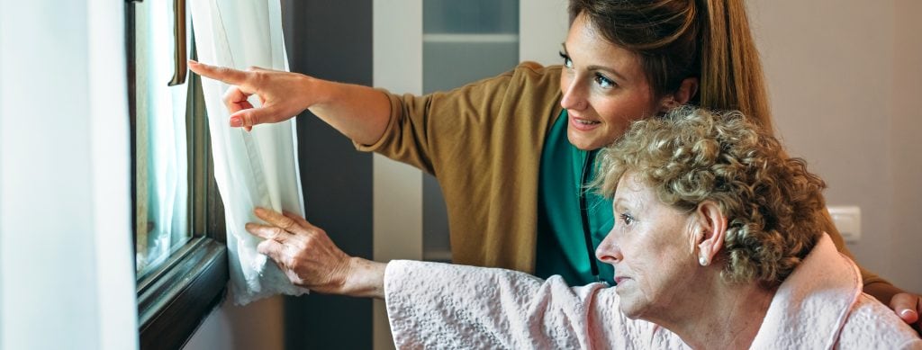 Caregiver showing the view through the window to elderly patient